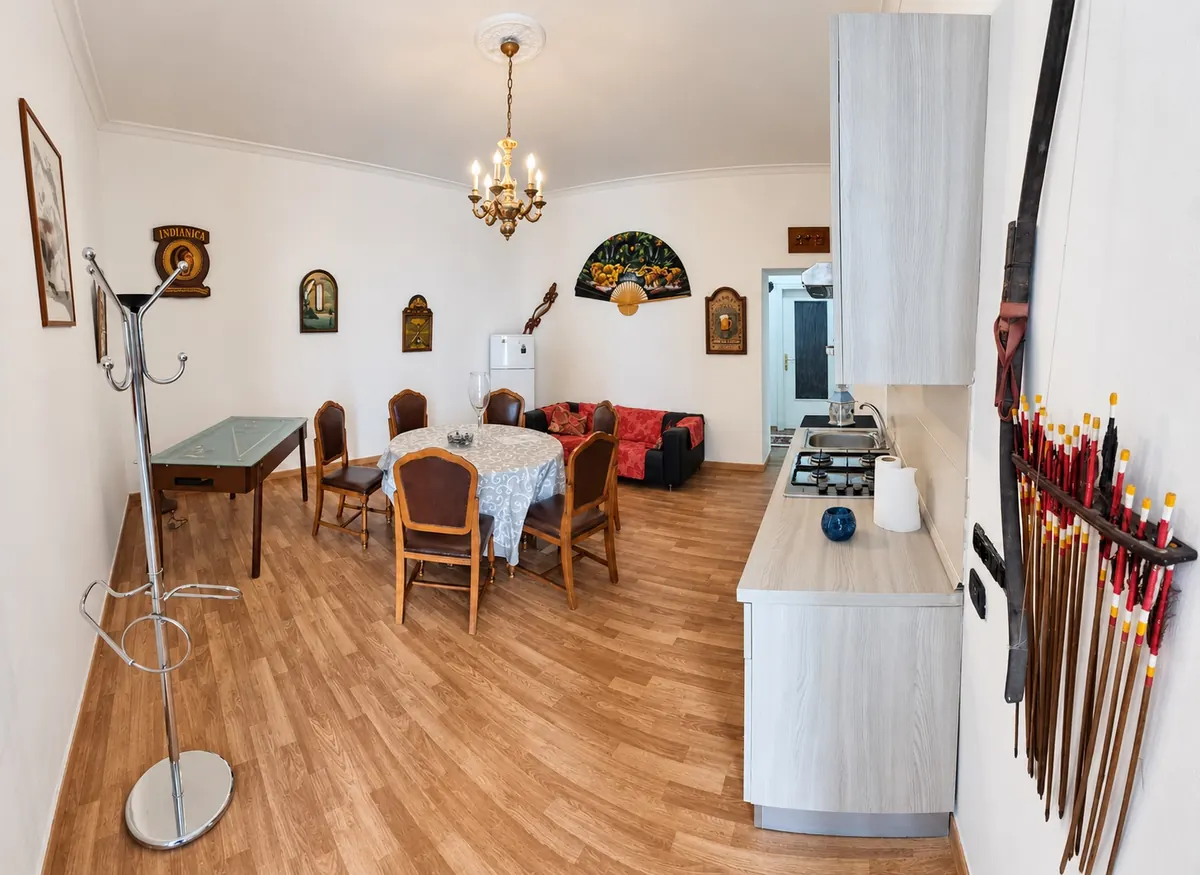 La sala da pranzo col tavolo rotondo, le sedie in legno e l'angolo cucina