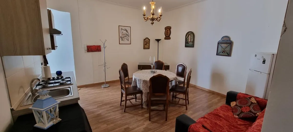 La sala da pranzo con l'angolo cucina e il divano rosso