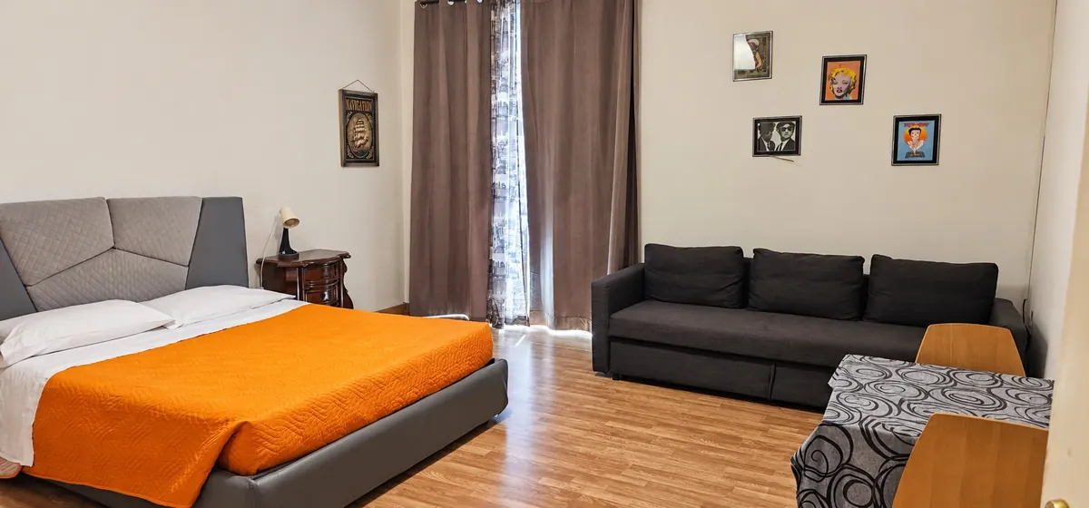 Camera matrimoniale col copriletto arancio e il divano nero