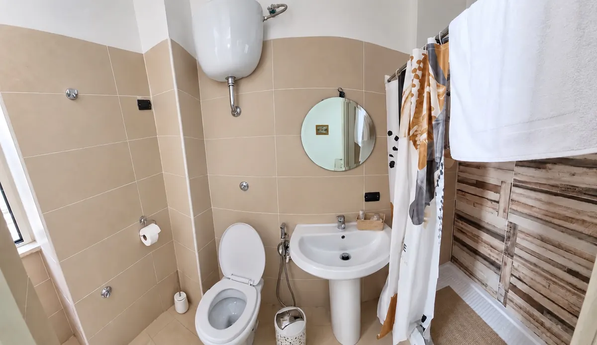 Bad mit Dusche, Waschbecken und rundem Spiegel