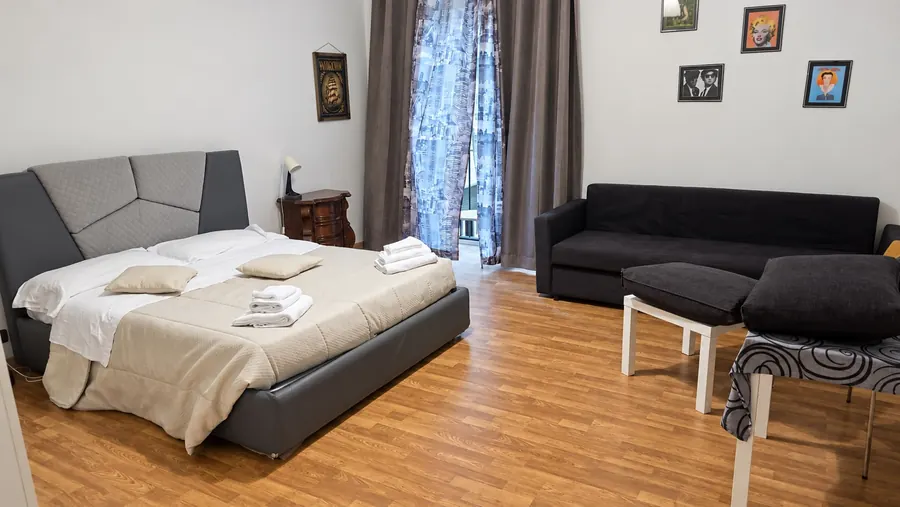 Habitación con cabecero gris, sofá negro y suelo de madera